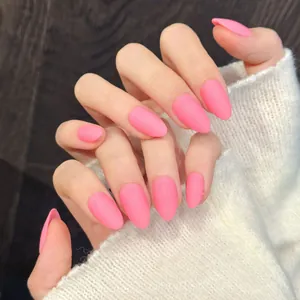 Hand wearing pink matte almond press-on nails with a minimalist solid fluorescent finish