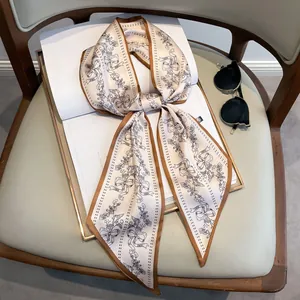 Eleganter elfenbeinfarbener Seidenschal mit Blumenmuster und braunem Rand auf Kunstbuch
