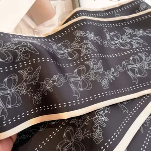 Detail eines schwarzen Seidenschals mit weißen Blumenmustern und eleganter Schrift