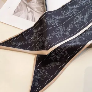 Detail eines schwarzen schmalen Seidenschals mit Goldpaspel und weißen Schleifenmustern
