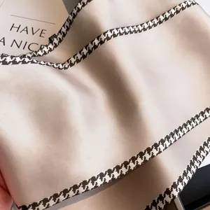 Detail of champagne silk scarf with black and white houndstooth border and satin finish