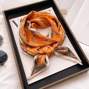 Vibrant orange silk scarf with luxury chain pattern and cream border on a black tray