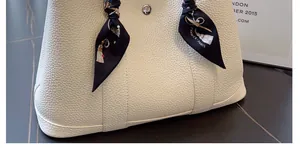Detalle de cinta de seda envuelta en el asa de un bolso tipo cubo de cuero granulado crema