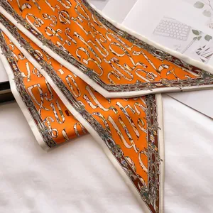 Macro detail of orange twilly silk scarf with white artistic letters and baroque floral patterns