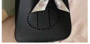 Detalle de bolso de cuero negro con diseño perforado y pañuelo de seda decorativo