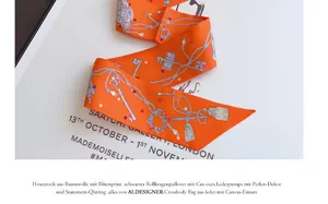 Primer plano de twilly de seda naranja con motivos de llaves vintage y cadenas para bolso