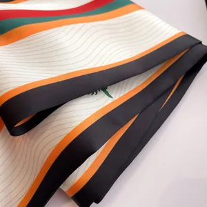 Détail macro du foulard en soie à rayures avec des motifs ondulés orange et vert