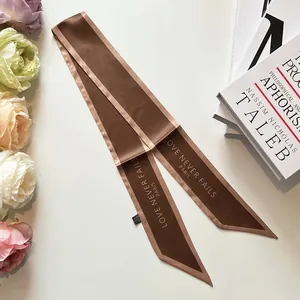 Detail of brown satin bag scarf with gold Paris slogan print and diagonal cut edges