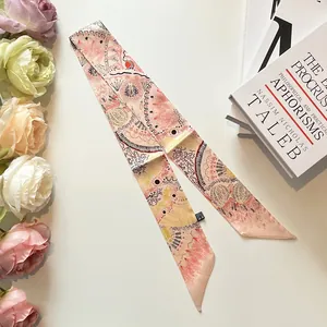 Petit foulard en soie rose pêche avec motifs abstraits posé sur un bureau blanc