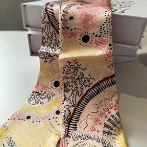 Détail d'un foulard étroit en soie crème avec motifs abstraits sur des boîtes cadeaux blanches