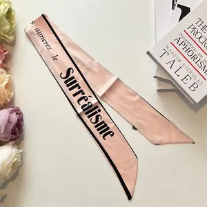 Dettaglio di un foulard in seta rosa con scritte francesi nere e accenti floreali