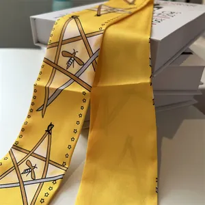Détail macro du twilly en soie jaune avec motifs d'abeilles et d'étoiles sur coffrets