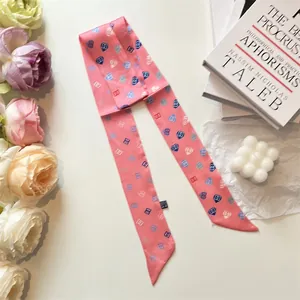 Close-up of pink silk twilly scarf with heart patterns on decorative books background