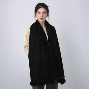 Détail d'une écharpe noire aspect cachemire avec des pompons décoratifs assortis