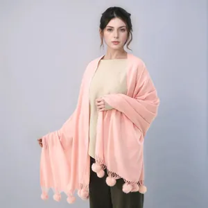 Détail d'une écharpe en cachemire rose clair avec pompons doux portée par un mannequin