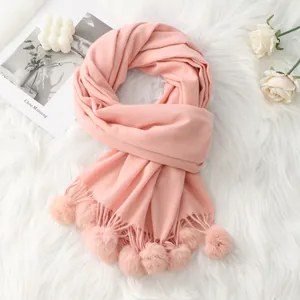Écharpe rose effet cachemire avec pompons assortis sur fond en peluche blanche