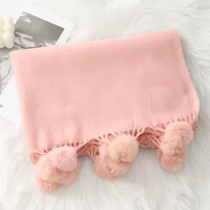 Écharpe rose effet cachemire avec pompons et franges sur un fond en peluche blanche