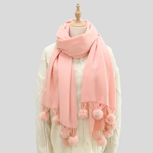 Vue détaillée d'une écharpe rose poudré avec pompons doux et finitions à franges fines