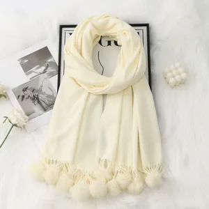 Détail d'une écharpe crème en cachemire synthétique avec des pompons doux et une maille fine