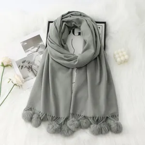 Détail d'écharpe grise effet cachemire avec pompons doux et franges sur tapis en fourrure