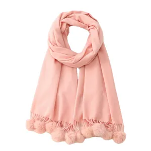 Écharpe rose avec pompons décoratifs et bordures à franges sur un fond blanc épuré