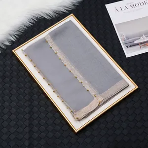 Détail d'une écharpe en soie grise avec bordure en perles dorées sur un plateau