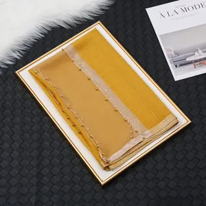 Détail d'une écharpe en soie gingembre avec bordure en perles dorées et texture froissée