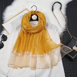 Détail d'une écharpe en soie jaune avec bordure en tulle et perles dorées fines