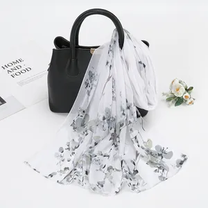 Détail d'une écharpe en mousseline imprimée fleurie drapée sur un sac à main en cuir noir