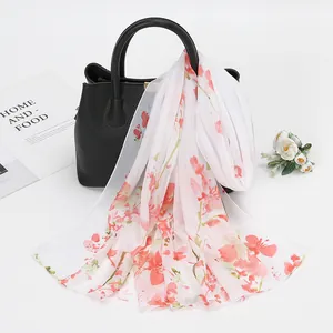 Détail d'une écharpe en mousseline fleurie drapée sur un sac à main en cuir noir