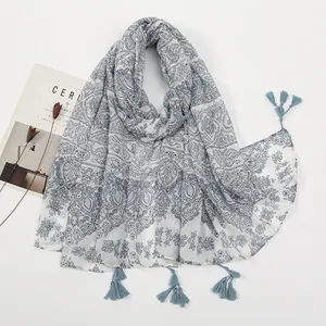 Detailed macro view of white linen-feel scarf featuring blue paisley floral patterns and tassels