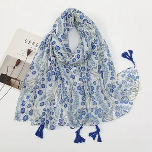 Close-up of white linen floral scarf with blue tassels and decorative magazine props