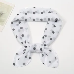 Detail of a thin chiffon square scarf with black polka dots tied in an elegant bow knot