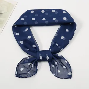 Detail of a navy blue chiffon scarf with white polka dots tied in a delicate bow knot