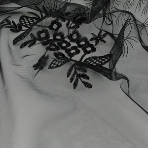 Détail du tissu en maille noire avec broderie florale délicate et texture ajourée