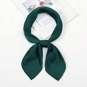 Close-up of a dark green satin scarf tied in a neat knot on an aesthetic magazine