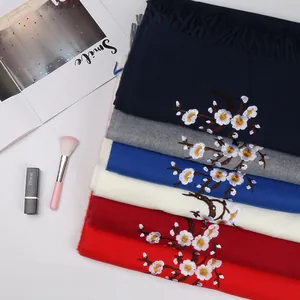 Detailed embroidery of white plum blossoms on soft cashmere-like fringed scarves in multiple colors