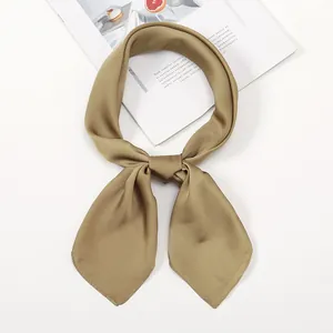 Detail of a khaki satin neck scarf tied in a bow on a white background with a magazine