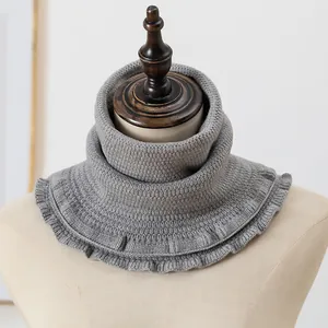 Macro detail of grey knitted neck warmer featuring a tiered collar and ruffled hem edges