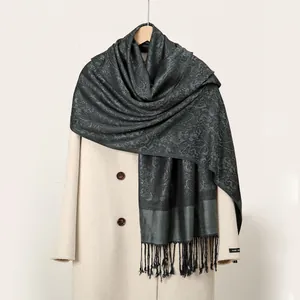 Détail de la texture jacquard paisley gris foncé et des franges sur l'écharpe longue