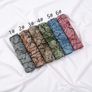 Close-up of lightweight branch print scarves in six vibrant colors neatly rolled on fabric