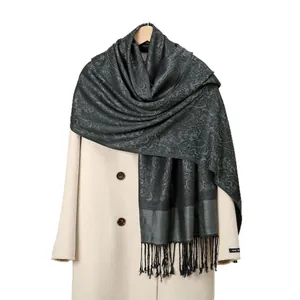 Écharpe en acrylique gris foncé à motif paisley avec pompons noirs sur un manteau