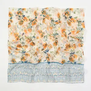 Détail d'un châle en voile avec imprimé marguerites orange et bleues sur fond beige