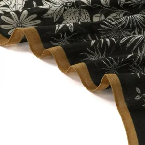 Close-up of linen fabric with palm leaf print and golden border on a black scarf