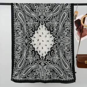 Detailed view of lightweight black and white paisley pattern scarf on a wooden hanger