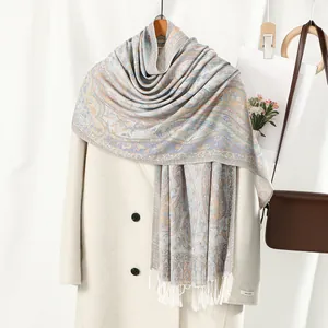 Elegant paisley jacquard scarf with white tassels paired with a beige wool coat and brown bag