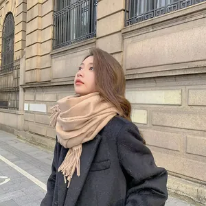 Donna elegante in cappotto nero con sciarpa calda beige effetto cashmere con frange