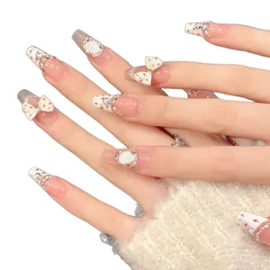 Faux ongles French avec nœuds 3D blancs, perles et étoiles sur une base rose nude