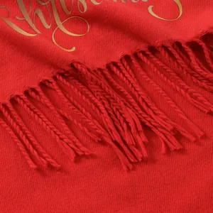 Detail of red Christmas scarf featuring golden cursive text and soft fringe tassels