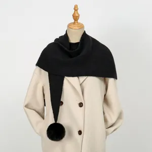 Detailansicht eines dicken schwarzen Strickschals mit Bommel auf einem beigen Mantel